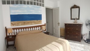 Un dormitorio con una cama grande, un aparador, un espejo y un cuadro con una escena de playa.