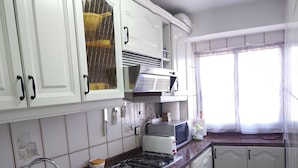 Una cocina con gabinetes blancos, encimera de granito, un lavamanos, estufa, microondas y una ventana con cortinas.