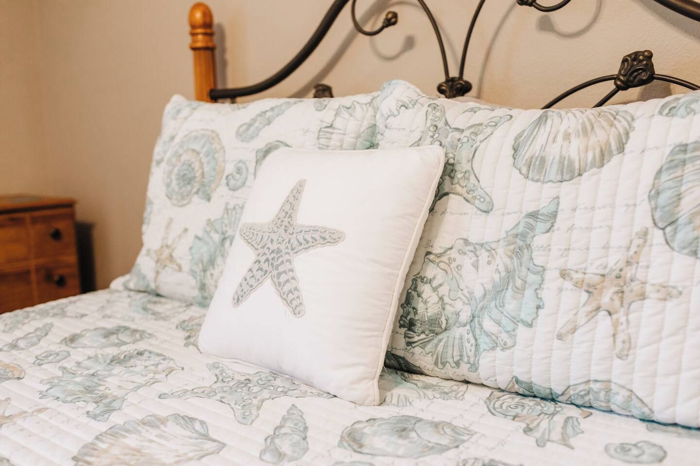 Un lit recouvert d’une courtepointe ornée de motifs représentant des créatures marines, avec une tête de lit en bois et une table de chevet placée à gauche.