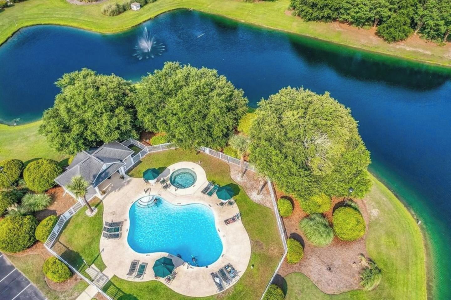 A large swimming pool with a hot tub, surrounded by a well-maintained lawn and trees.