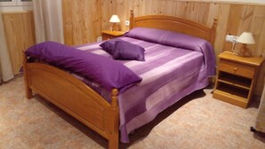 A bedroom with a wooden bed, purple bedding, a nightstand with a lamp, and a wall-mounted picture. - Villa Paraiso for Large Families (Alcanar)