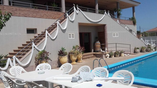 A poolside area with a staircase leading to a covered entrance, surrounded by potted plants and white outdoor furniture. - Villa Paraiso for Large Families (Alcanar)