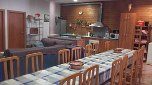 A dining area with a long table set for multiple people, surrounded by wooden chairs. A kitchen with a stove and sink is visible in the background. - Villa Paraiso for Large Families (Alcanar)