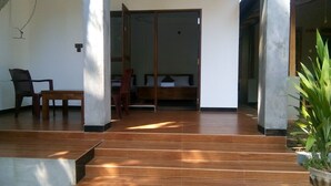 A room with a wooden floor, a bed with a wooden headboard, a chair, and a table. - Umesh Home Stay (Dambulla)