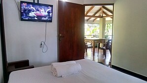 A hotel room with a bed, a TV mounted on the wall, and an open door leading to an outdoor area with a table and chairs. - Umesh Home Stay (Dambulla)
