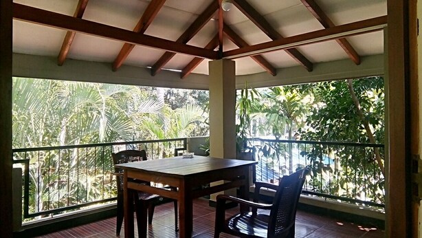 A covered balcony with a wooden table and chairs, surrounded by lush tropical foliage. - Umesh Home Stay (Dambulla)