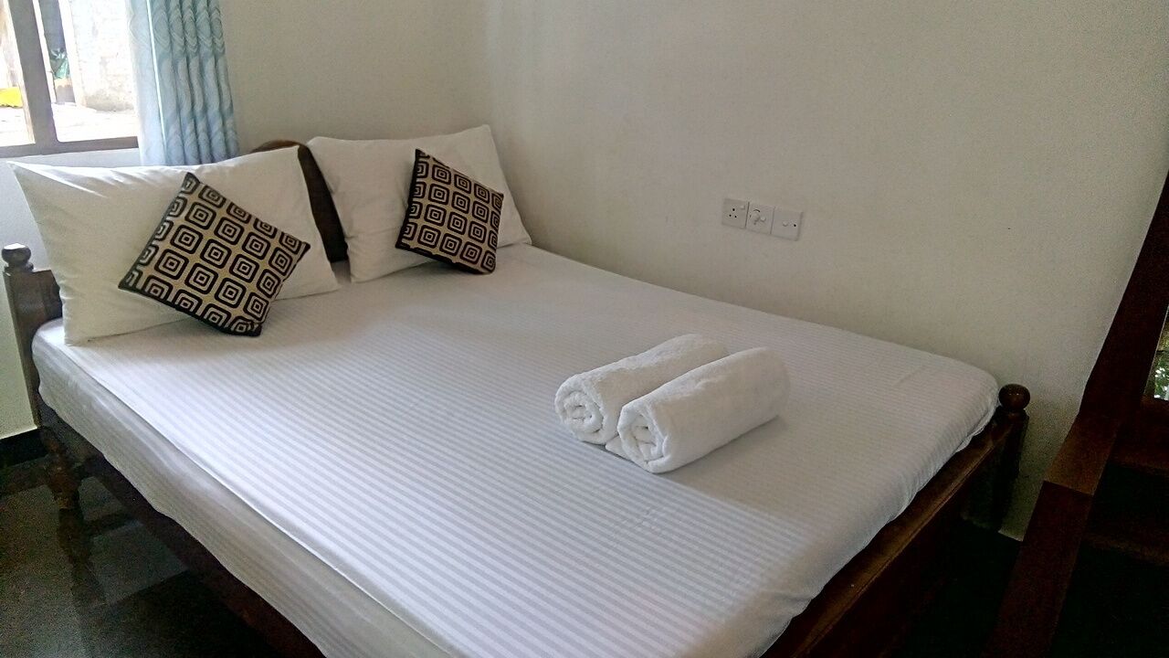 A neatly made bed with white linens, two patterned pillows, and two rolled towels.