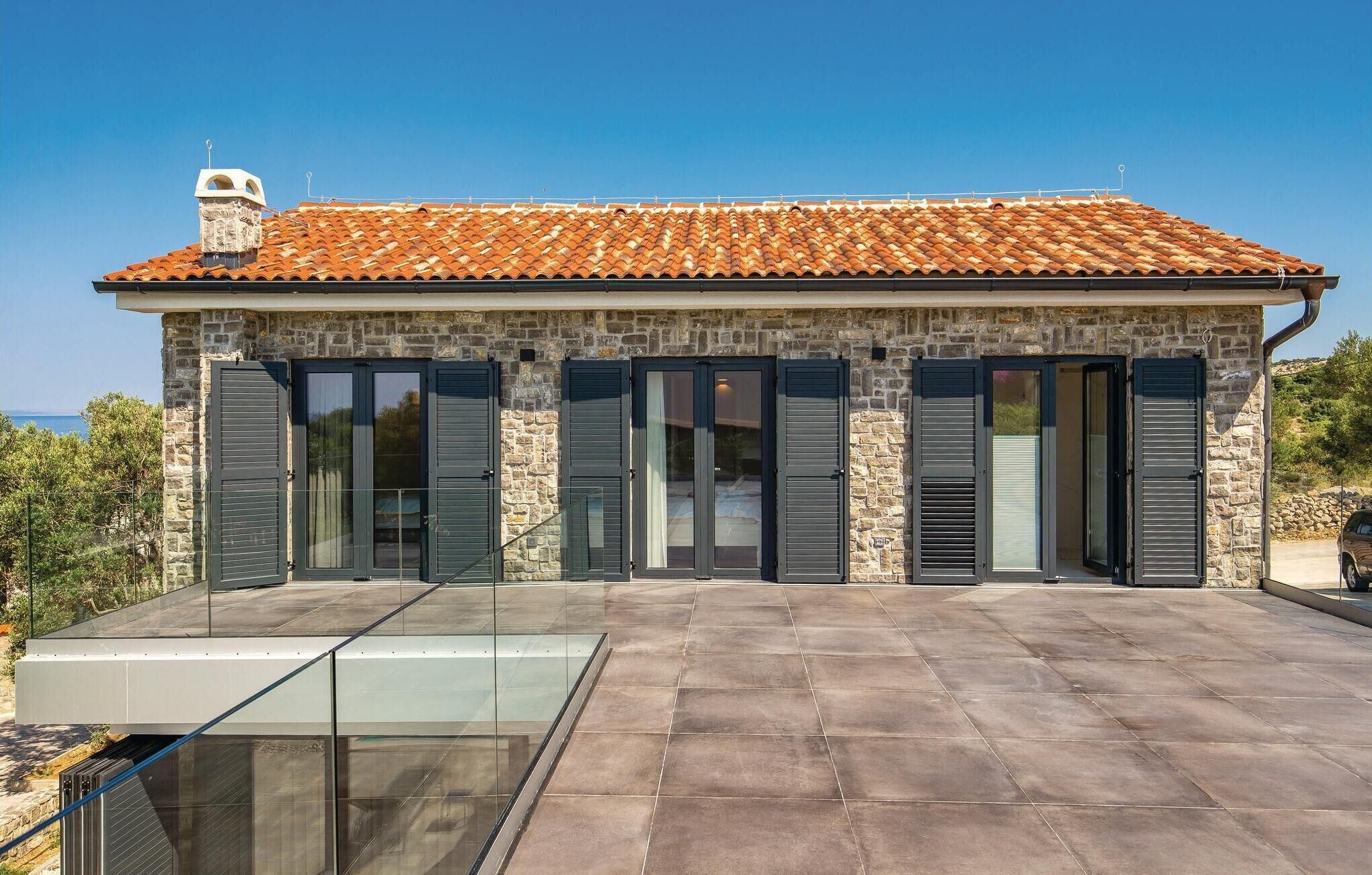 Un edificio de piedra con techo de tejas, ventanas amplias y un balcón de cristal.