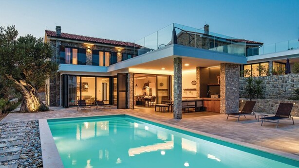 Een modern huis met twee verdiepingen, een zwembad, stenen muren en een glazen balkon.