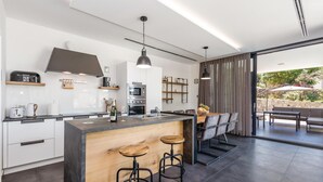Een moderne keuken met een centraal eiland, barstoelen en een eethoek met uitzicht op de omgeving.