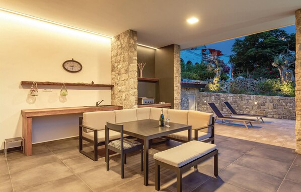 A modern outdoor dining area with a stone wall, a wooden table, and a bench. - Beautiful home in Lun (Lun)