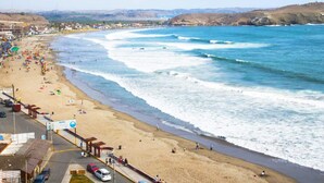 Una playa con una carretera que corre paralela a la orilla, algunos coches aparcados y una vista despejada del océano.