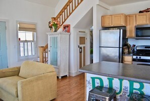 A spacious kitchen with wooden cabinets, a stainless steel refrigerator, and a dining area with a beige sofa. - Frisky Fish cottage on the water (Machiasport)