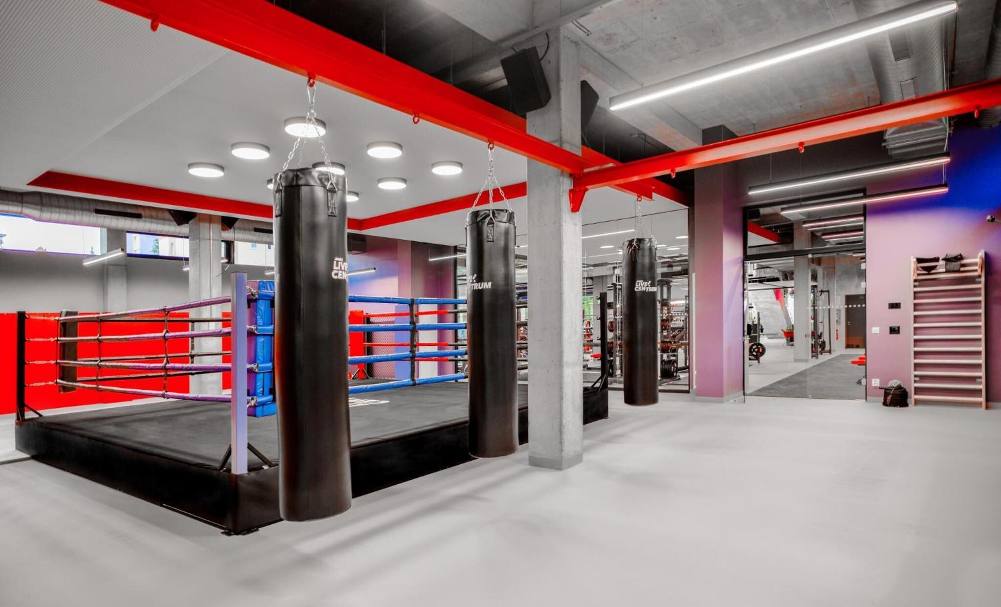A boxing ring with heavy bags and a red and blue padded area.