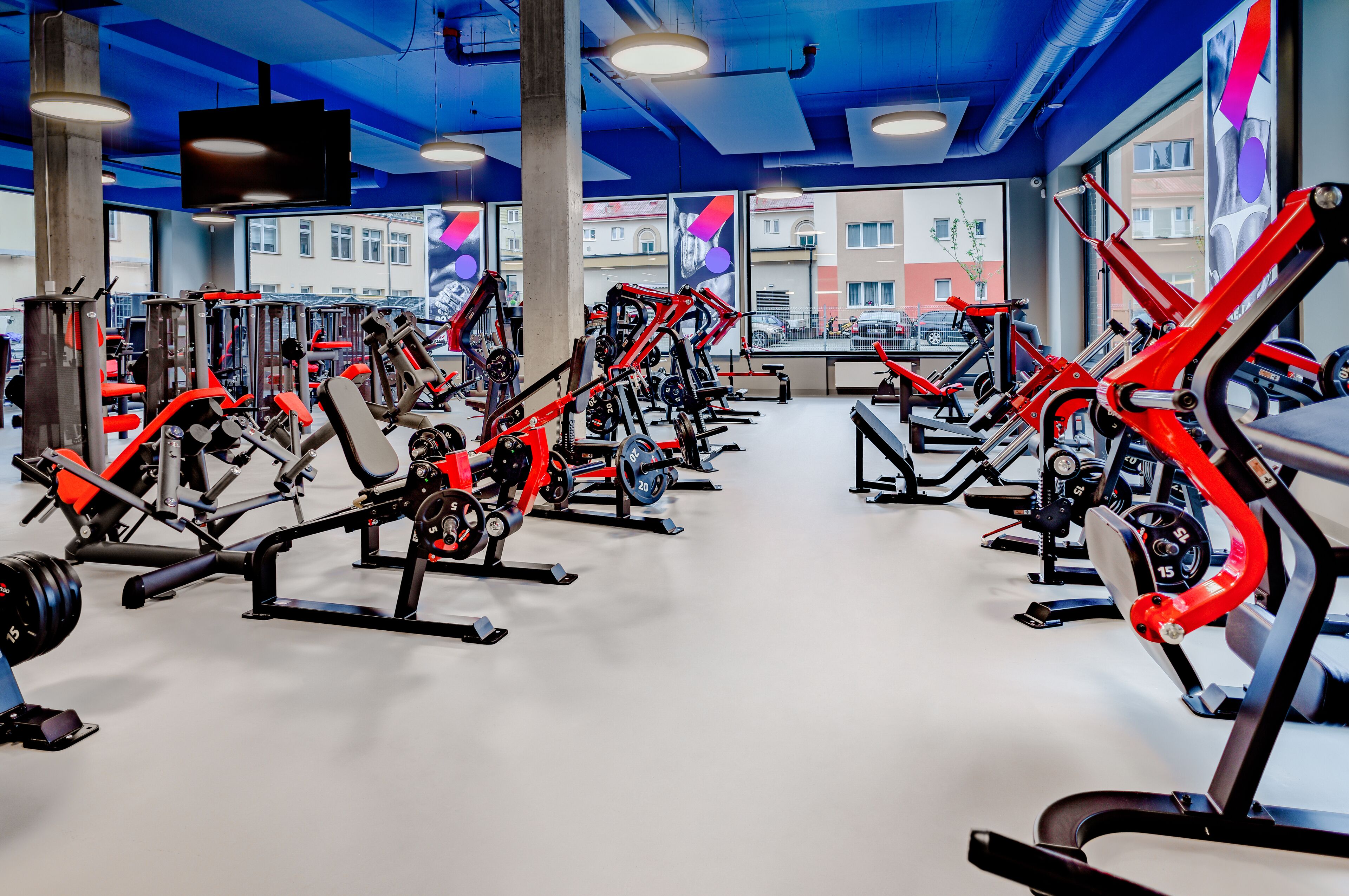 A gym with various exercise machines, large windows, and a blue ceiling.