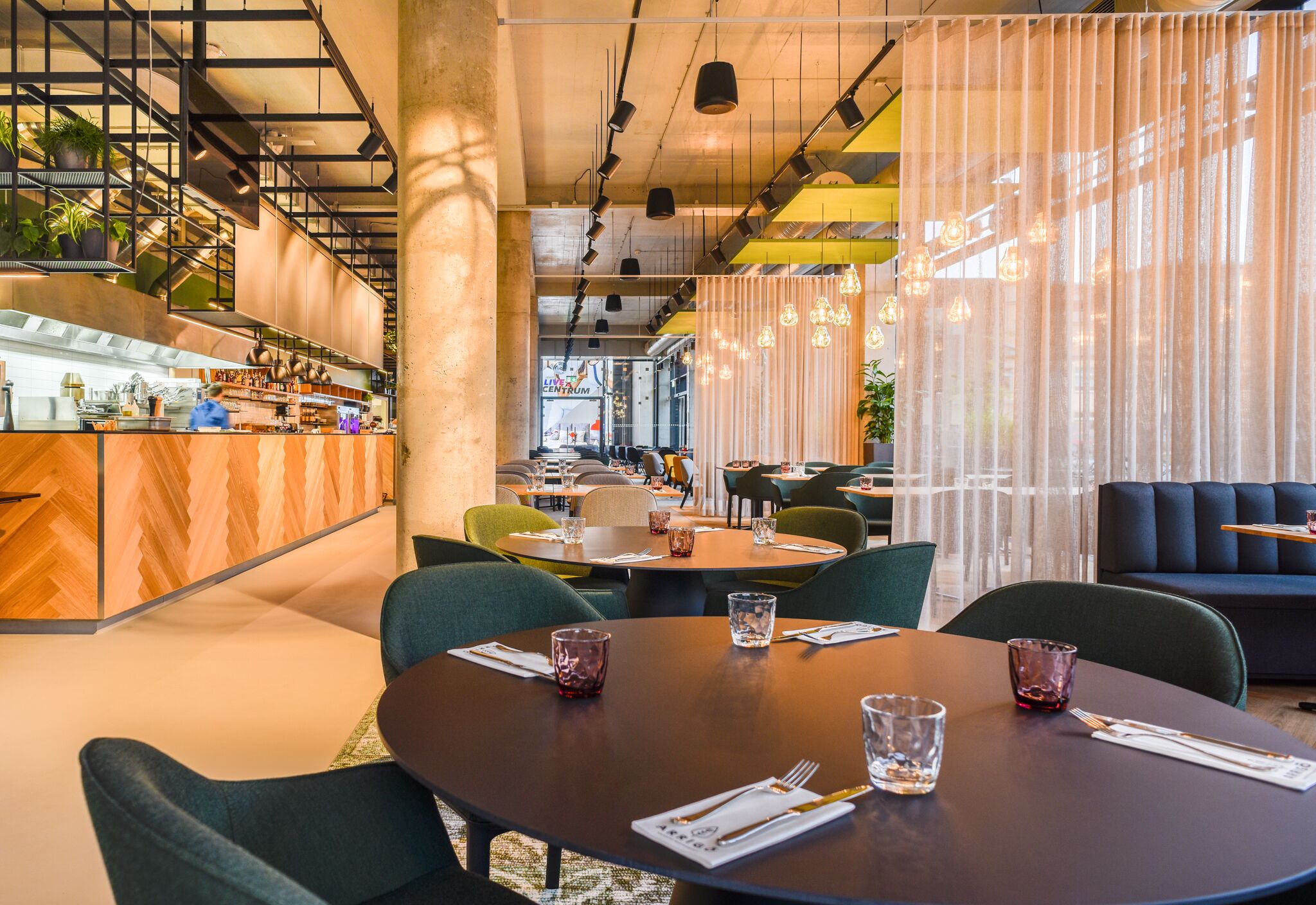A modern restaurant with round tables, green chairs, and a bar area with wooden counter.