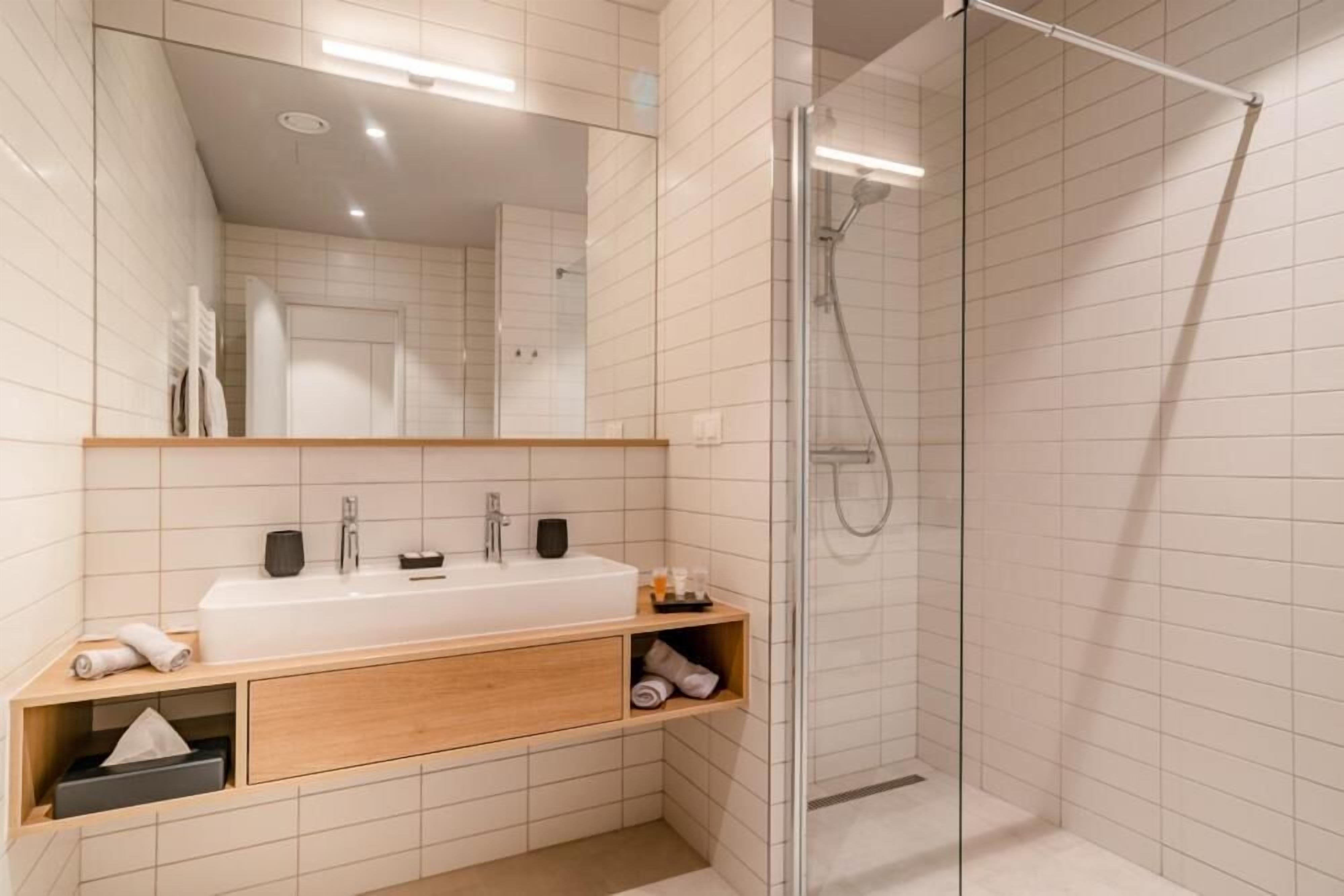 A modern bathroom with a large mirror, a white sink, and a glass-enclosed shower.