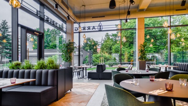 Moderni ravintola, jossa on suuret ikkunat, mustat istuimet ja katosta roikkuvat valaisimet.