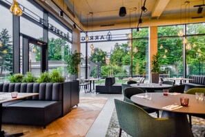 Ein modernes Restaurant mit großen Fenstern, schwarzen Sitzgelegenheiten und hängenden Leuchten.
