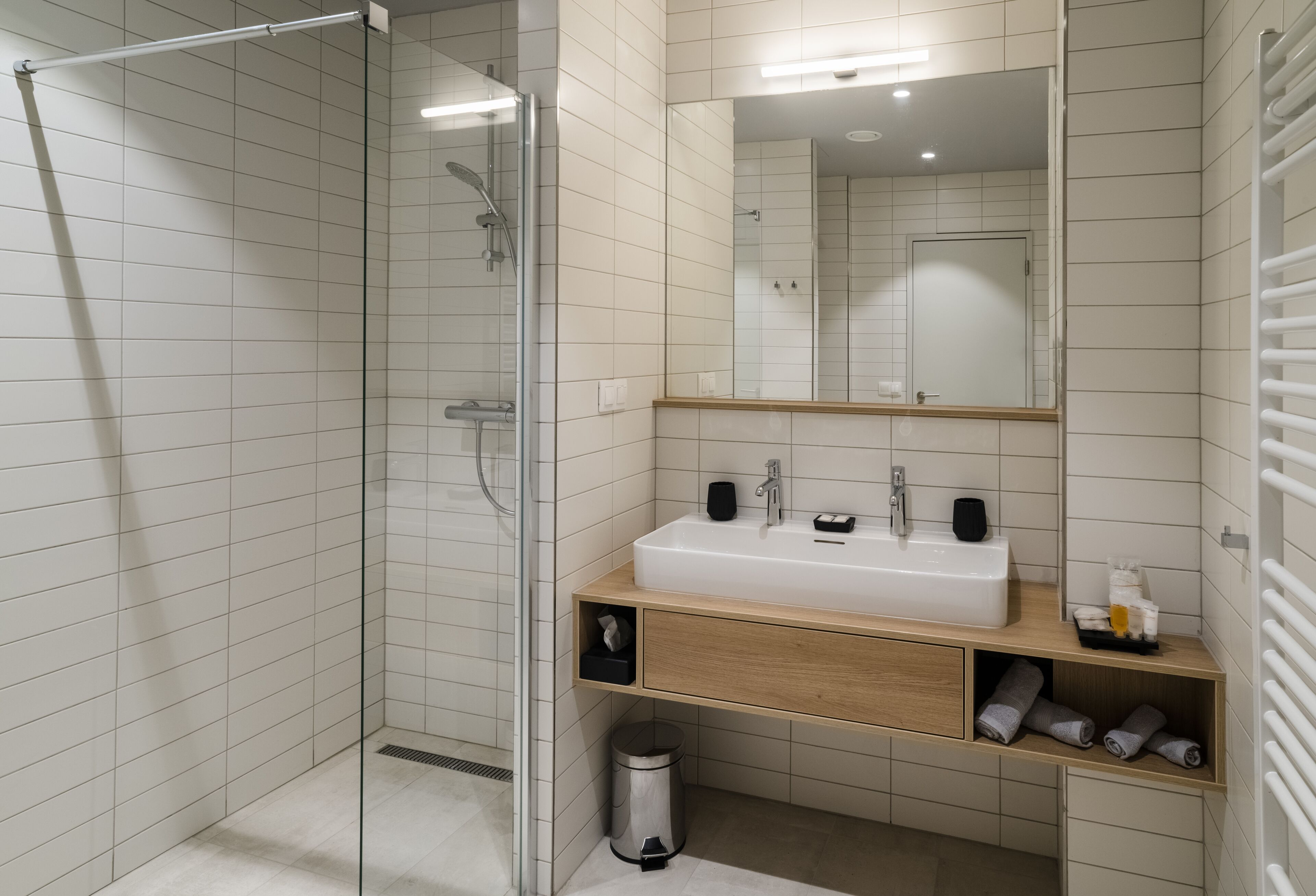 Un baño moderno con cabina de ducha de vidrio, un lavabo blanco con encimera de madera y un espejo sobre el lavabo.