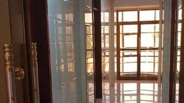 A hallway with a tiled floor leading to a room with a large window. - Kigala Hotel (Dar es Salaam)