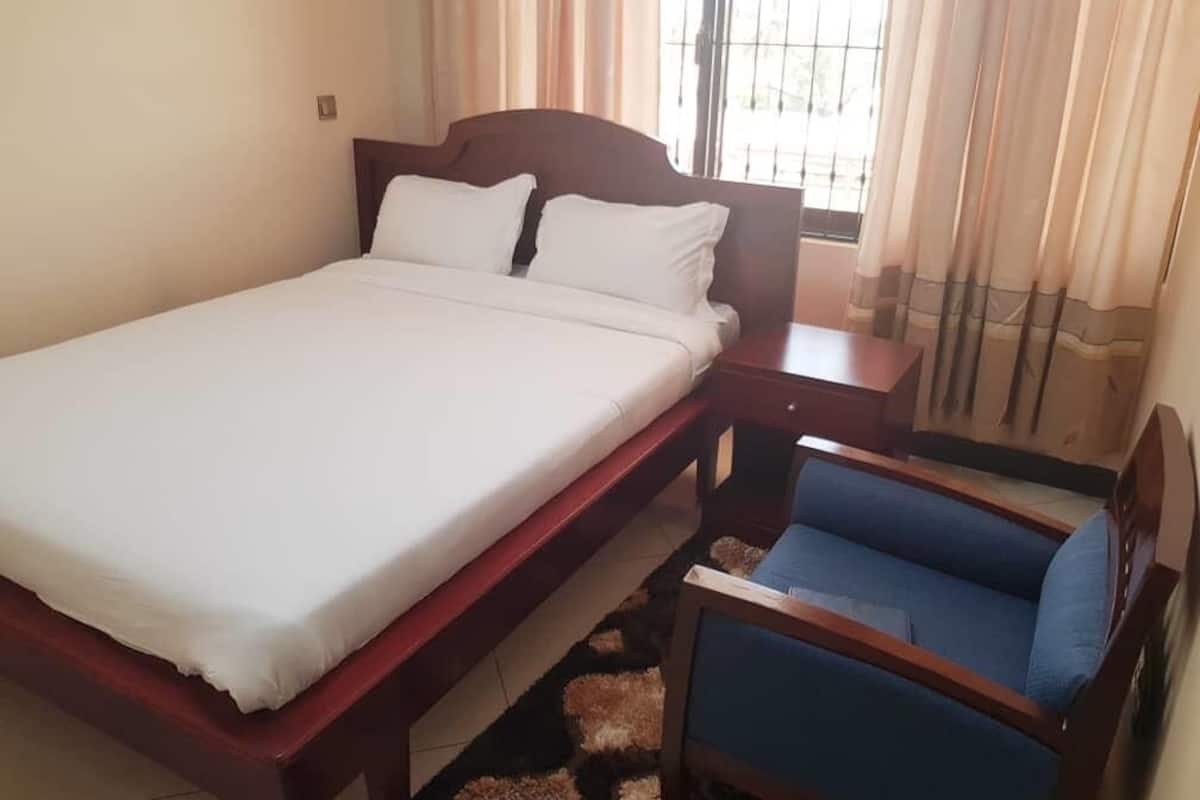 Un dormitorio con una cama grande, una mesita de noche de madera, una silla azul y una ventana con cortinas.