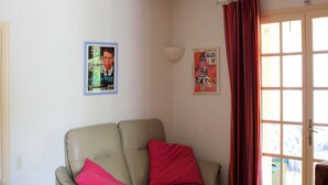 A living room with a beige sofa, a glass coffee table, and a door with a red curtain. - in Bagnols-en-Forêt, quiet, with large swimming pool (Bagnols-en-Forêt)