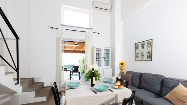 A dining area with a table set for two, a grey sofa, and a staircase. - Tenuta Capizucchi (Rome)