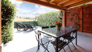 An outdoor patio with a wooden pergola, a table with chairs, and a view of a green hedge and a white flower wall. - Tenuta Capizucchi (Rome)