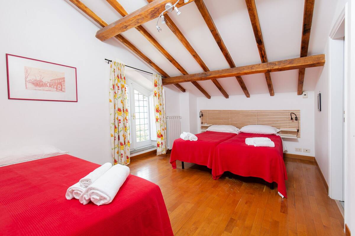 A room with two beds, wooden beams, a window with curtains, and a framed picture on the wall.