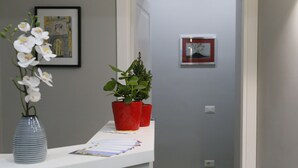 A reception desk with a vase of white orchids, two red potted plants, and framed artwork on the wall. - Porta San Gennaro (Naples)