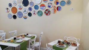 A dining area with two tables, each with a green tablecloth and white chairs. The walls are decorated with a variety of plates and bowls. - Porta San Gennaro (Naples)