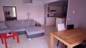 Een woonkamer met een grijze bank, een rode salontafel en een houten eettafel.