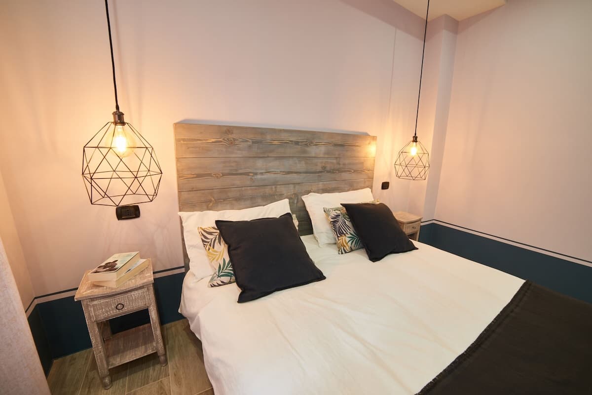 A neatly made bed with a wooden headboard, two bedside tables, and geometric pendant lights.