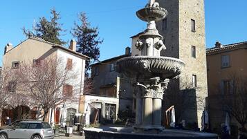 A stone fountain with a tiered design in a square, surrounded by buildings with traditional architecture.