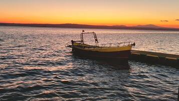 Ein Boot liegt an einem Steg, im Hintergrund ruhiges Wasser und ein Sonnenuntergang.