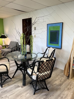 A modern dining area with a glass table surrounded by black chairs, a green wall, and a blue framed artwork.