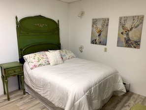 A bedroom with a green headboard, floral bedding, and two deer paintings on the wall.