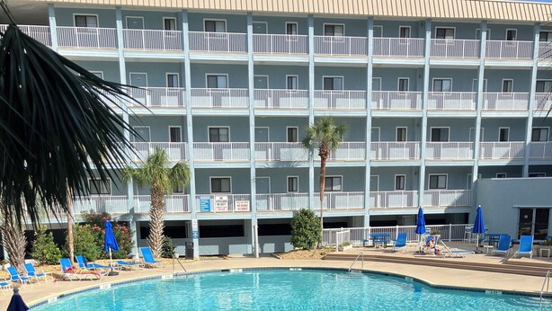 Un hotel con zona de piscina, sillones de descanso y sombrillas.