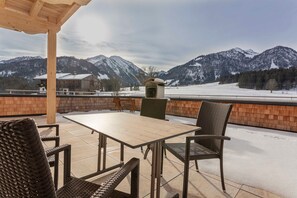 Um alpendre coberto com mesa e cadeiras, uma parede de tijolos e vista para montanhas cobertas de neve.