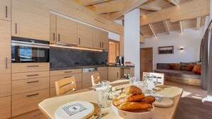 Eine moderne Küche mit Holzschränken, ein Essbereich mit Tisch für vier Personen und eine Wohnbereich mit Sofa und Kissen.