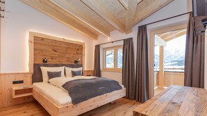 Ein hölzernes Bett mit Kopfteil, ein Nachttisch und Blick auf Berge durch ein Fenster.