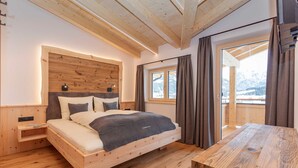 Ein schlicht eingerichtetes Schlafzimmer mit Holzbett, Nachttischen und Blick auf verschneite Berge.