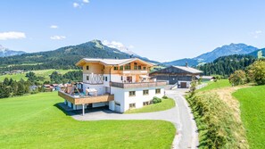 Un chalet de dos pisos con balcón, un patio cubierto y vistas de las montañas circundantes.