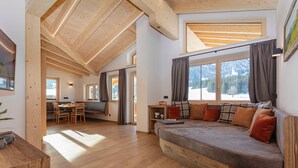 Un interior moderno con techo de madera, un sofá con cojines, zona de comedor y ventanas amplias.