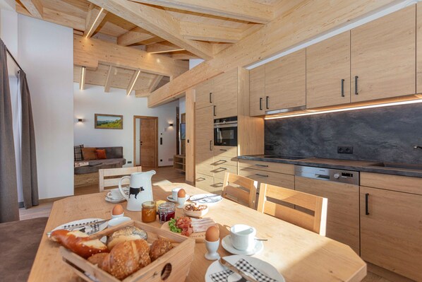 A modern kitchen with wooden cabinets, a dining table set with breakfast, and a view of the living area.