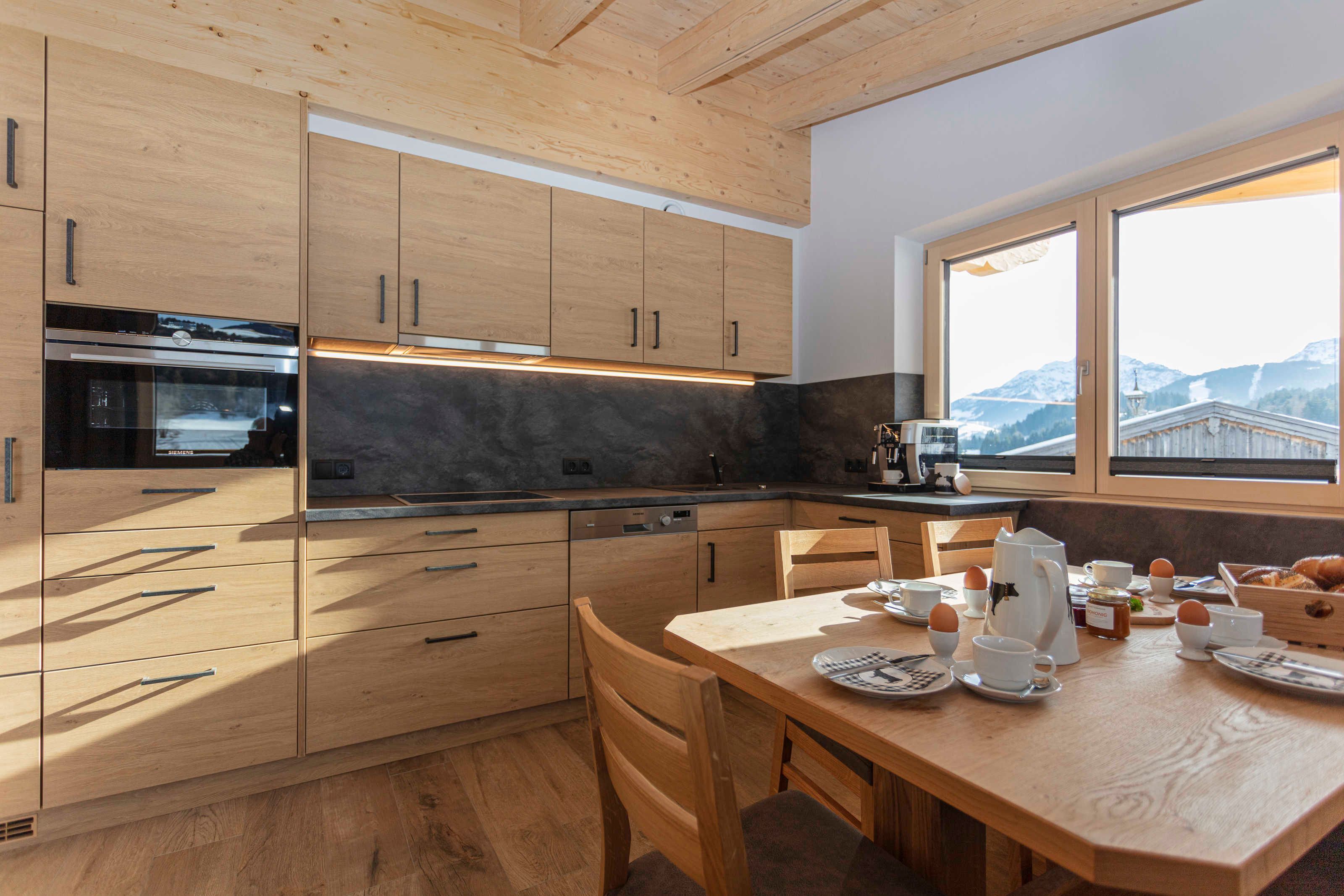 Eine moderne Küche mit Holzschränken, einem eingebauten Backofen und einer Essecke mit gedecktem Tisch zum Frühstück.