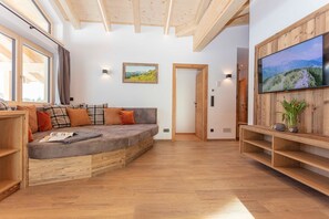 A modern living room with a built-in sofa, wooden beams, a television, and a scenic landscape painting.