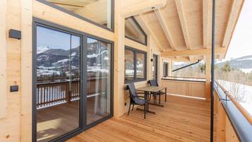 Une terrasse en bois avec une table et des chaises, de grandes portes-fenêtres coulissantes et une vue sur des montagnes enneigées.