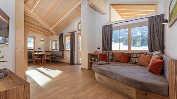 Un intérieur moderne avec un plafond en bois, un canapé avec des coussins, un coin repas et de grandes fenêtres.
